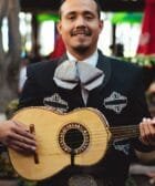 Man in Black Charro Holding a Brown Acoustic Guitar