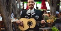 Man in Black Charro Holding a Brown Acoustic Guitar